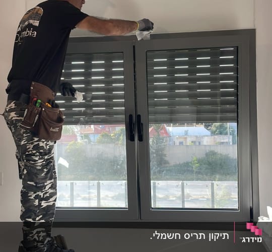 אדם על סולם מתקין תריסים בחלון